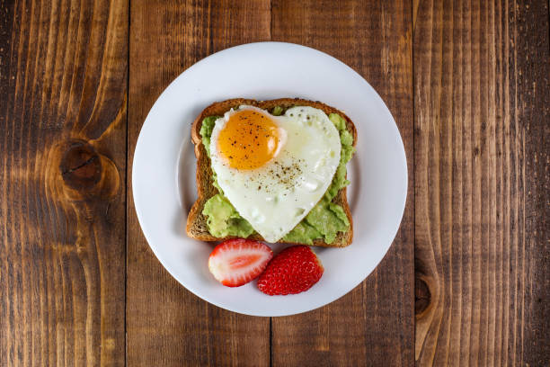 brinde com abacate e ovo em forma de coração - eggs breakfast heart shape fried egg - fotografias e filmes do acervo