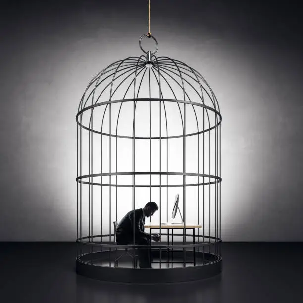 pondered businessman sitting by the worktop in metal birdcage at concrete wall background