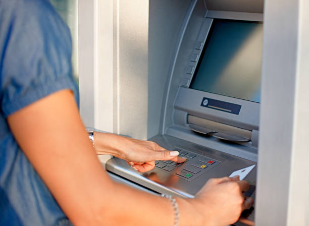 istock Woman using ATM holding card and pressing the PIN security number on the keyboard automatic teller machine 1046728756