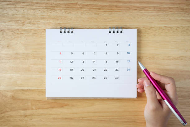 istock calendar page on table with female hand holding pen, top view 1046812436