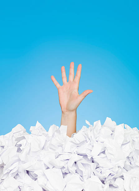 Image of person buried in paper leaving one hand out Human Buried in white papers on blue background drowning photos stock pictures, royalty-free photos & images