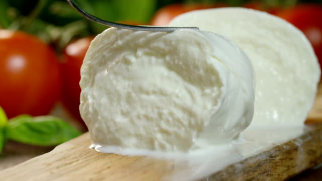 macro shot of a fresh Italian mozzarella di bufala and bio full of milk and the background with red tomatoes and basil.