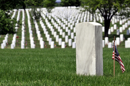 One gravestone in the front with copyspace, and endless rows of military graves continuing behind the green hill on Arlington National Cemetery in Virginia, decorated with US flags on Memorial Day. Narrow DOF.