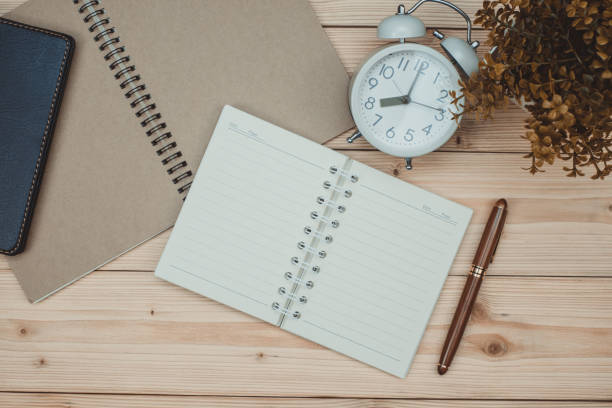 istock Office supplies or office work essential tools items on wooden desk in workplace, pen with notebook and alarm clock, top view 1046888668