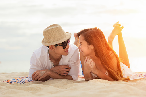 Asian couple lying Honeymoon at sunset tropical beach in Thailand