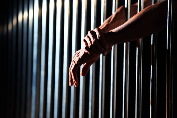 istock close up of prisoner hands in jail. 1046928648