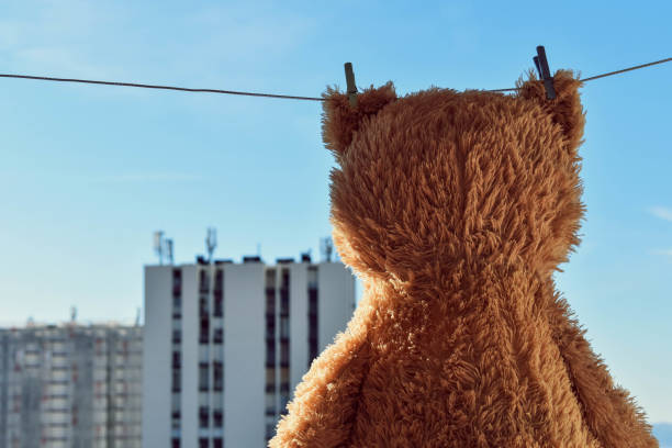 istock Cute brown stuffed toy Teddy Bear hanging on a clothesline with high building view 1046934962