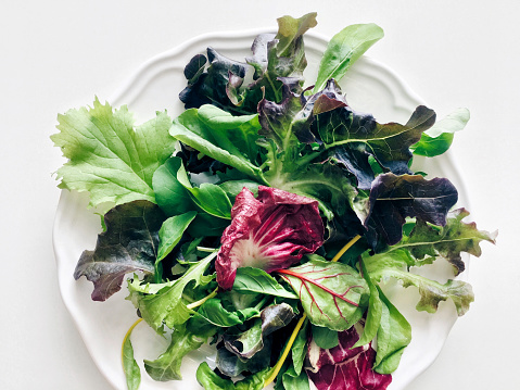 Mixed fresh salad leaves on a white background, top view