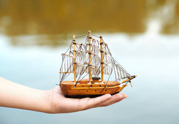 child playing with a toy sailing ship by the river, hand closeup