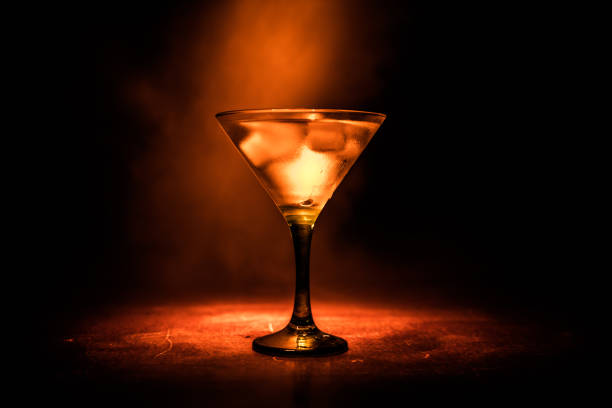 martini in feuer-konzept. glas des berühmten cocktail martini brennen bei feuer im dunkel getönten nebligen hintergrund. - martini brand vermouth stock-fotos und bilder