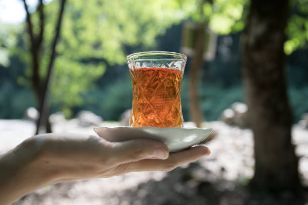 Eastern black tea in glass on woman`s hand at forest. Eastern tea concept. Armudu traditional cup. Green nature background. Selective focus