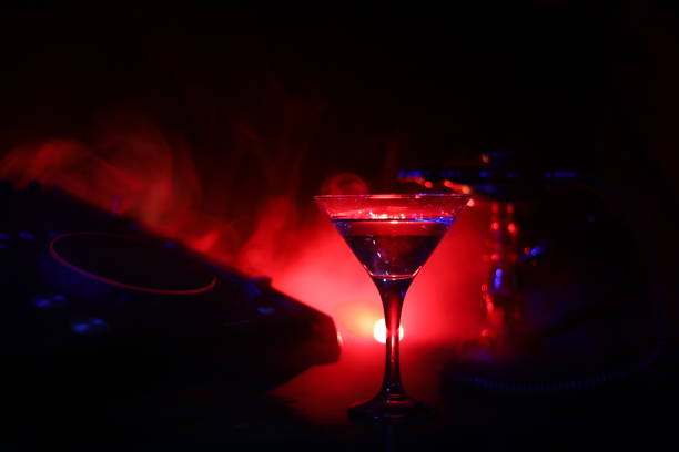 istock Glass with martini with olive inside on dj controller in night club. Dj Console with club drink at music party in nightclub with disco lights. 1046960828