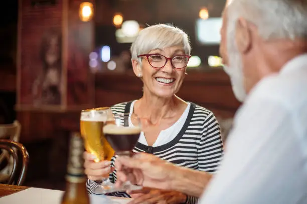 Active senior couple having a good time in the bar and drinking beer.