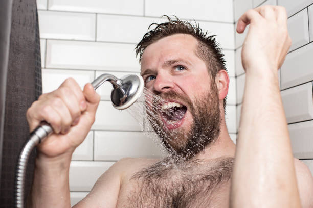 Bearded man singing in the bathroom using the shower head with flowing water instead of a microphone.