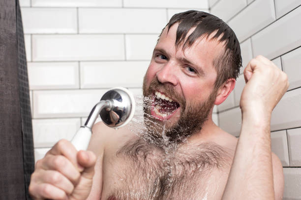 istock Bearded man singing in the bathroom using the shower head with flowing water instead of a microphone. 1047010176