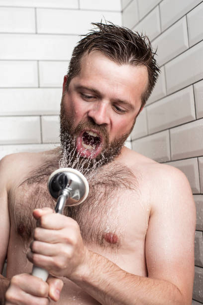 istock Bearded man singing in the bathroom using the shower head with flowing water instead of a microphone. 1047010208