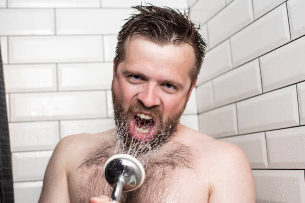 istock Bearded man singing in the bathroom using the shower head with flowing water instead of a microphone. 1047010216