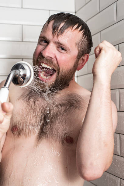 istock Bearded man singing in the bathroom using the shower head with flowing water instead of a microphone. 1047010232