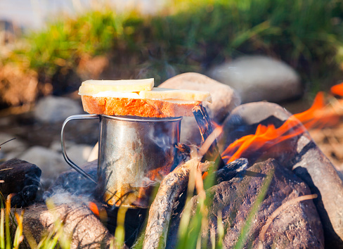 Warming up a cup of tea with cheese butterbrot (sandwich) at campfire in wild camping