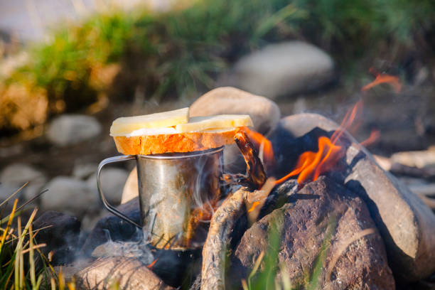 Warming cup of tea with cheese butterbrot (sandwich) on burning campfire at wild camping