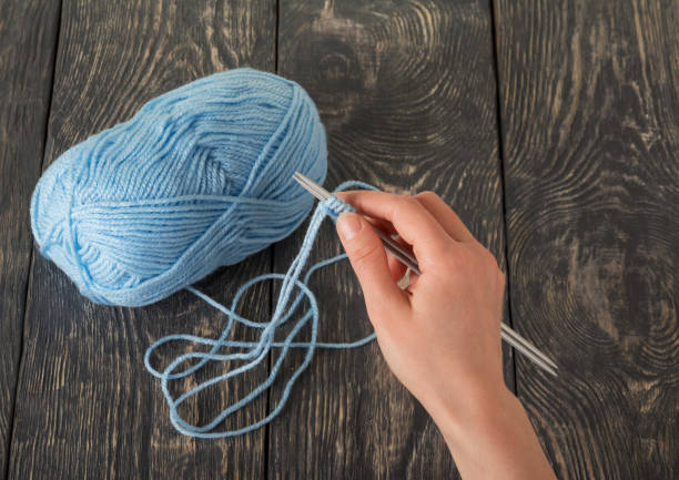 istock Female hand holds a crochet hook for blue wool thread on dark boards 1047023408