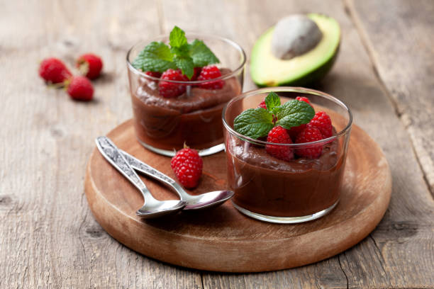 avocado chocolate mousse avocado chocolate mousse with raspberries in glass serving glasses on an old wooden background avocado brown stock pictures, royalty-free photos & images