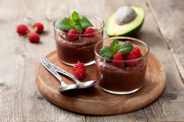 avocado chocolate mousse with raspberries in glass serving glasses on an old wooden background