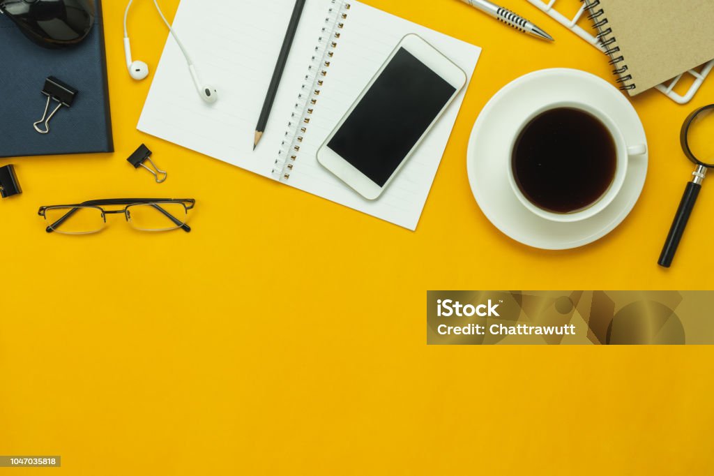 Table top view aerial image of accessories office desk background concept.Flat lay of variety object the mobile phone & pen and coffee with earphone on modern rustic yellow paper with copy space. Top - Garment Stock Photo