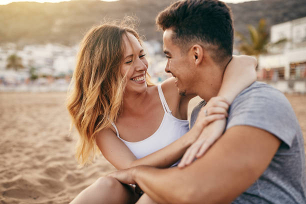 istock Romantic young couple sitting together on a beach at sunset 1047058864