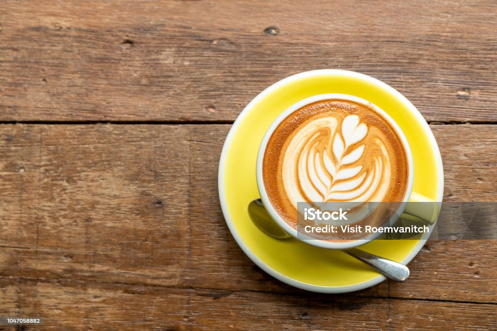 Draufsicht der heißen Cappuccino Kaffee in einer gelben Schale mit Latte Art auf Holztisch Hintergrund. - Lizenzfrei Kaffee - Getränk Stock-Foto
