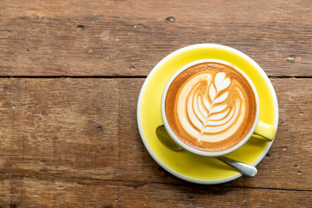 draufsicht der heißen cappuccino kaffee in einer gelben schale mit latte art auf holztisch hintergrund. - cappuccino fotos stock-fotos und bilder