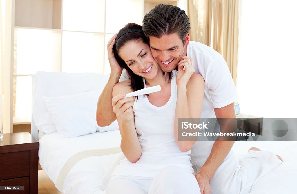 Enamored couple finding out results of a pregnancy test Enamored couple finding out results of a pregnancy test sitting on the bed Pregnancy Test Stock Photo