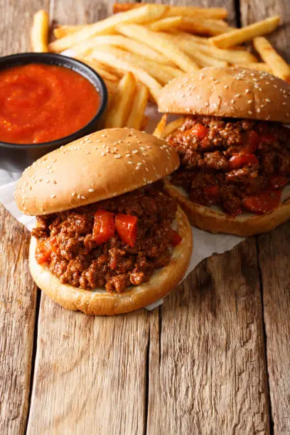 Tasty Sloppy Joe sandwiches with beef and French fries, ketchup closeup on the table. vertical
