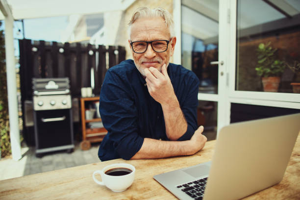 Smiling senior man sitting outside working on a laptop