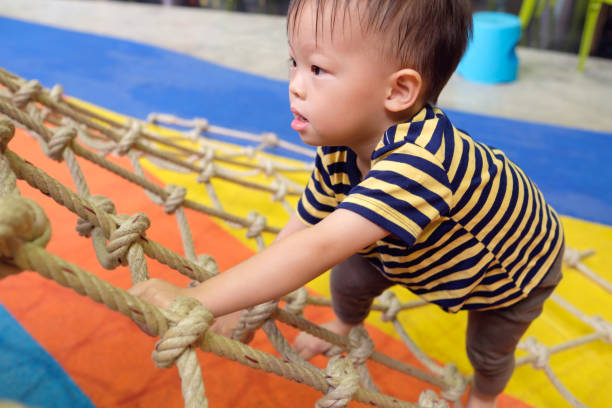 かわいい小さなアジア 2 歳幼児赤ちゃん男の子の子供楽しい屋内遊び場でジャングルジ��ムに登るしようとすると、 - brain gym ストックフォトと画像