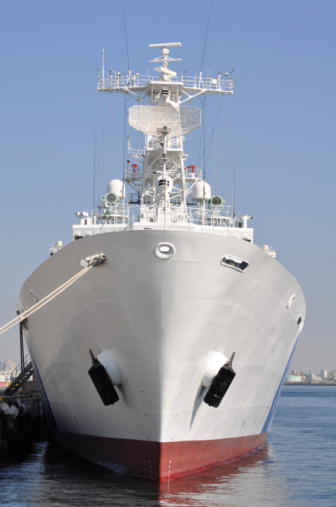 Front view of a guard boat of the Japan Coast Guard moored at the port in Yokohama,  Japan.  The hull of the ship is painted in white. It is equipped with antennas and radars.