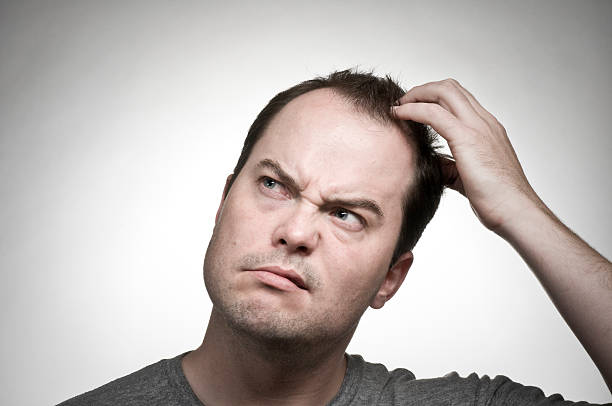 Man scratching his head and looking confused stock photo