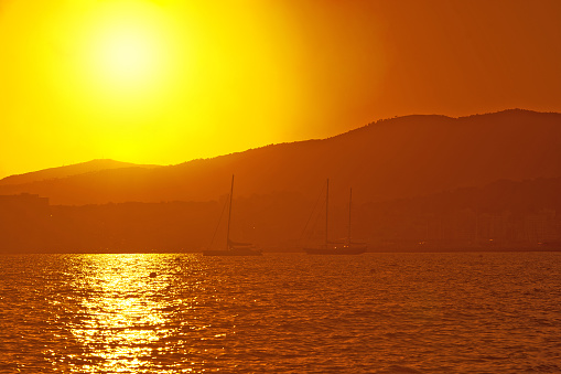 Sailing yachts in golden haze at sunset on a beautiful afternoon in September in Mallorca, Spain.