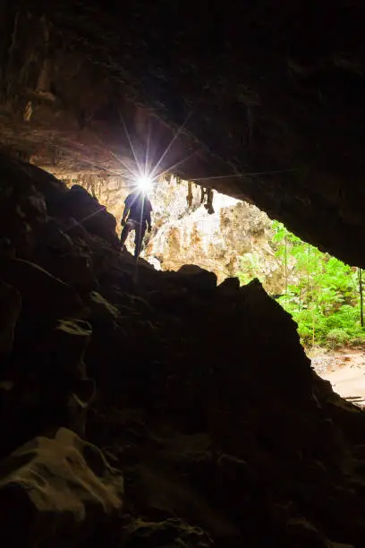 Photo of Young man exploring mystery cave with a torch, Phraya Nakhon Cave is a large cave which has a hole in the ceiling allowing sunlight to penetrate, the cave is most popular attraction at Prachuap Khiri Khan, Thailand.
