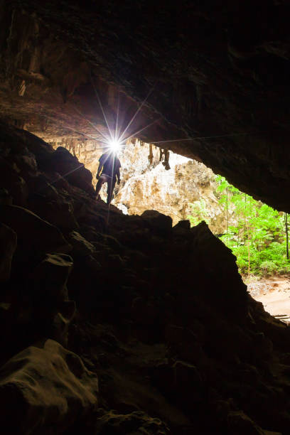 young man exploring mystery cave with a torch, phraya nakhon cave is a large cave which has a hole in the ceiling allowing sunlight to penetrate, the cave is most popular attraction at prachuap khiri khan, thailand. - phraya nakhon cave imagens e fotografias de stock