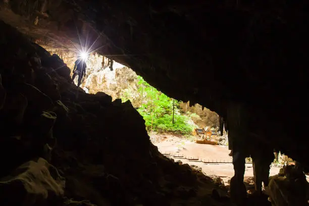 Photo of Young man exploring mystery cave with a torch, Phraya Nakhon Cave is a large cave which has a hole in the ceiling allowing sunlight to penetrate, the cave is most popular attraction is a pavilion constructed during the reign of King Rama. Prachuap Khiri K