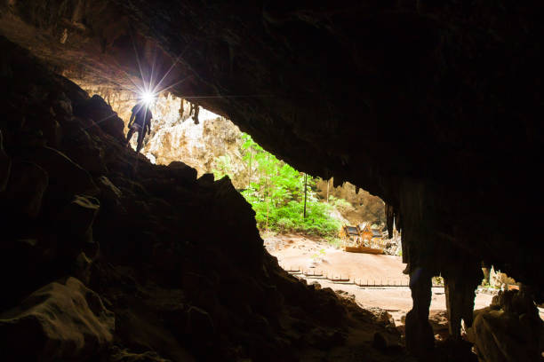 young man exploring mystery cave with a torch, phraya nakhon cave is a large cave which has a hole in the ceiling allowing sunlight to penetrate, the cave is most popular attraction is a pavilion constructed during the reign of king rama. prachuap khiri k - phraya nakhon cave imagens e fotografias de stock