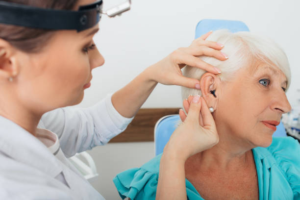 istock doctor helping elderly woman inserting hearing aid 1047136796