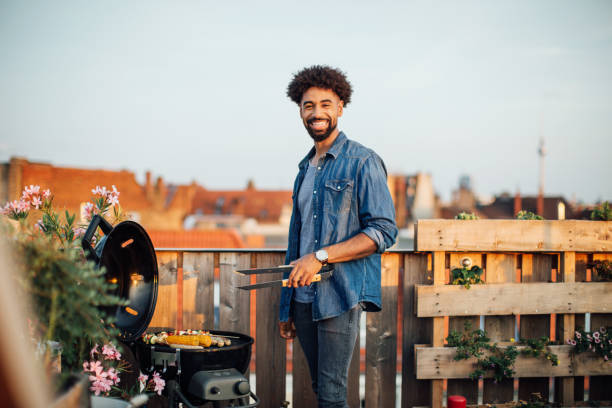 jeune homme de cuisson sur la grille du barbecue à partie sur le toit - grilled photos et images de collection