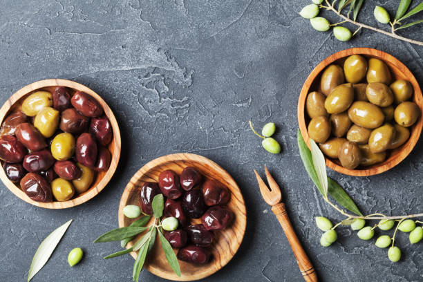 istock Natural olives in bowls with olive branch on black stone table top view. 1047162822