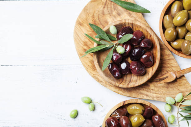 istock Olives in wooden bowls decorated with fresh olive tree branch on white kitchen table top view. 1047162868
