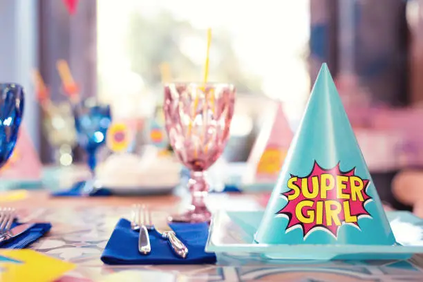 Super girl. Laconic photo of blue party hat fo super girl placed on the plate near the glasses