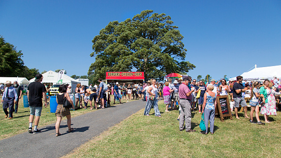 Gower, UK: August 05, 2018: Spectators enjoying an Agricultural Show during the summer months in Wales. A burger stall is selling fast food to the tourists. Panoramic format with blue sky.