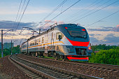 Passenger electric train moves against the background of green trees and evening sky