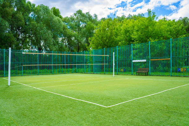 vista sobre o parque de esportes no parque com grama artificial e uma rede esticada sobre um fundo de árvores verdes e céu nublado - badminton court - fotografias e filmes do acervo